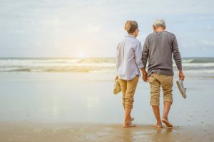 Senior Couple Walking On The Beach Holding Hands At Sunrise
